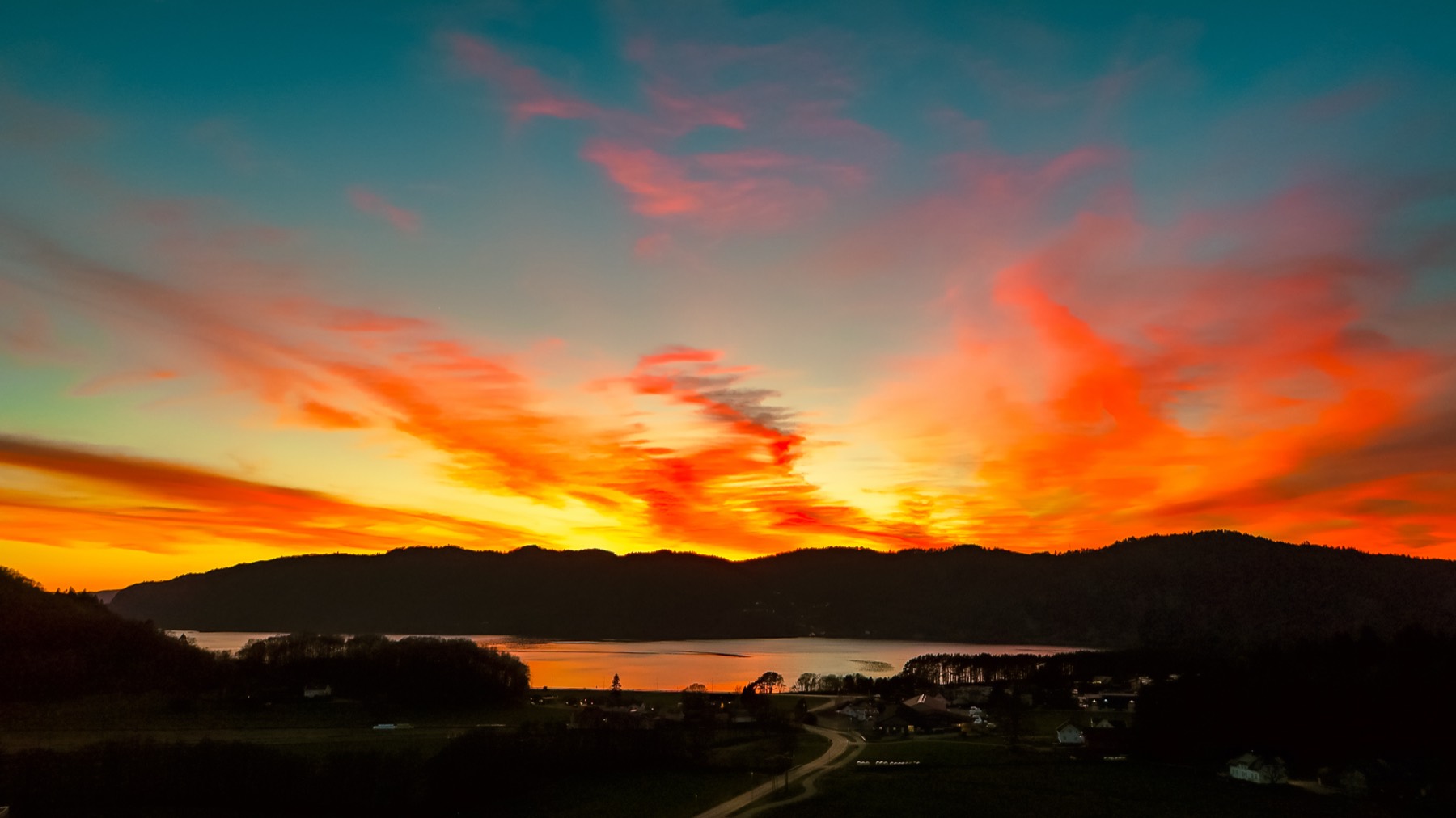 Kvavik i Lyngdal sett fra lufta i solnedgang, med oransje og rød himmel over fjorden